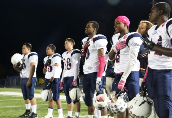 The Oilers line up and say the Pledge of Allegiance in the Hercules Titans' stadium before kickoff. Pops of pink stood out on many of the players who wore the color in honor of Breast Cancer Awareness. (Photo by: Jennifer Baires)